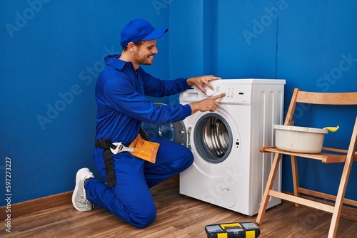 Young hispanic man technician turning on washing machine at laundry room