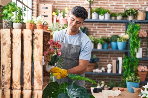 Young hispanic man florist smiling confident holding plant at flower shop