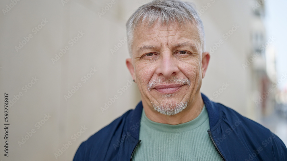 Middle age grey-haired man standing with serious expression at street Middle age grey-haired man standing with serious expression at street