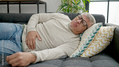 Middle age grey-haired man suffering for stomach ache lying on sofa at home © Krakenimages.com