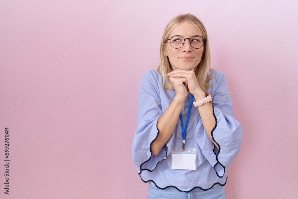 Young caucasian business woman wearing id card laughing nervous and excited with hands on chin looking to the side Young caucasian business woman wearing id card laughing nervous and excited with hands on chin looking to the side