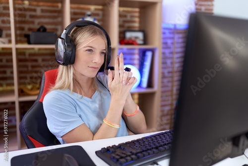 Young caucasian woman playing video games wearing headphones holding symbolic gun with hand gesture, playing killing shooting weapons, angry face
