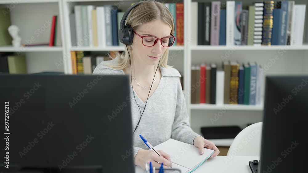 Young blonde woman using computer taking notes at library university Young blonde woman using computer taking notes at library university