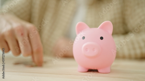 Young arab man inserting coin on piggy bank sitting on table at home