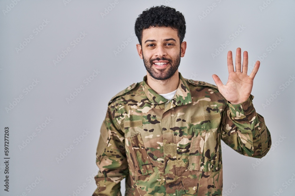Arab man wearing camouflage army uniform showing and pointing up with fingers number five while smiling confident and happy. Arab man wearing camouflage army uniform showing and pointing up with fingers number five while smiling confident and happy.