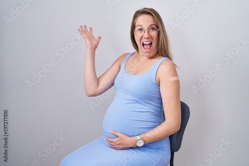 Young pregnant woman wearing band aid for vaccine injection celebrating victory with happy smile and winner expression with raised hands