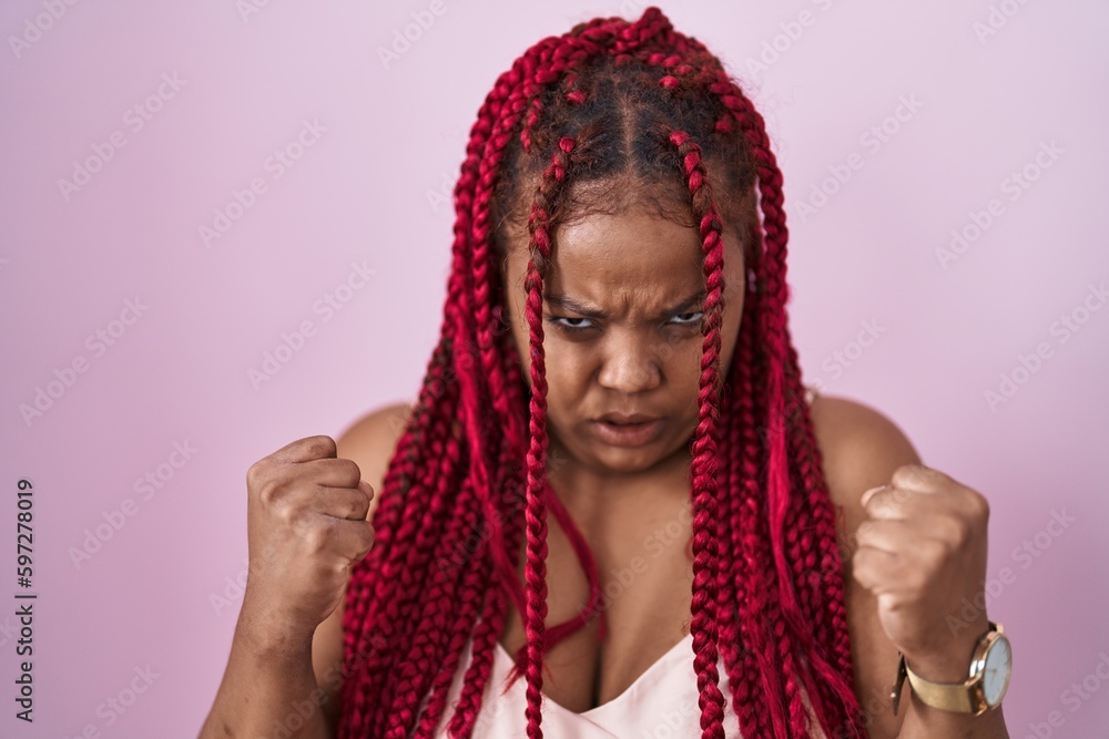 African american woman with braided hair standing over pink background angry and mad raising fists frustrated and furious while shouting with anger. rage and aggressive concept. African american woman with braided hair standing over pink background angry and mad raising fists frustrated and furious while shouting with anger. rage and aggressive concept.