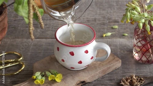 Pouring herbal tea into a ceramic cup, with fresh primula flowers in the foreground