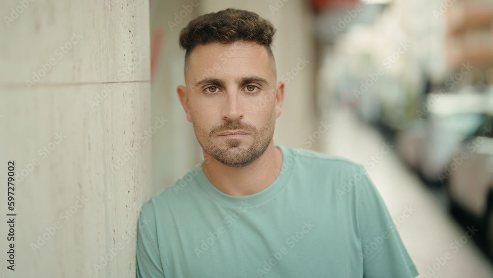 Young hispanic man standing with serious expression at street