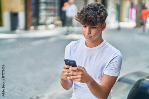 Young hispanic teenager using smartphone with relaxed expression at street