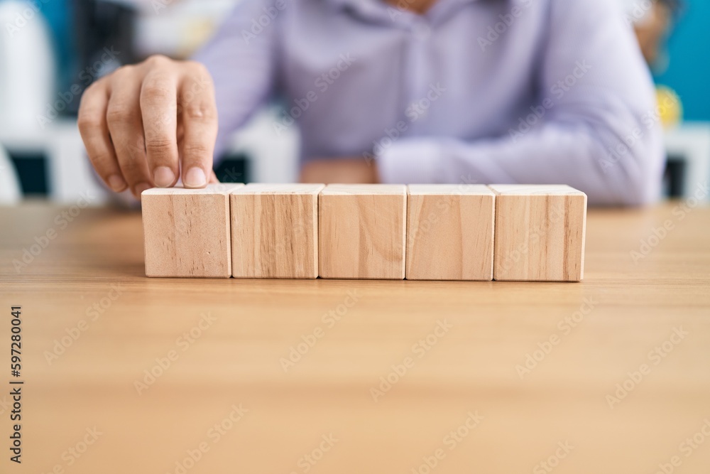 Young hispanic man business worker sitting on table with wooden cubes at office Young hispanic man business worker sitting on table with wooden cubes at office