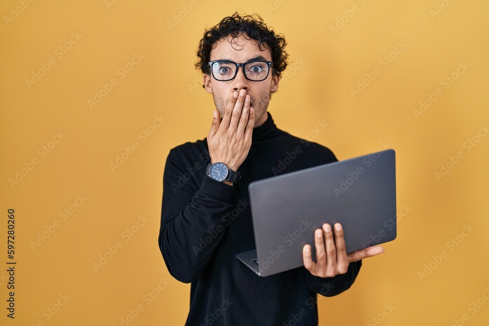 Hispanic man working using computer laptop covering mouth with hand, shocked and afraid for mistake. surprised expression Hispanic man working using computer laptop covering mouth with hand, shocked and afraid for mistake. surprised expression