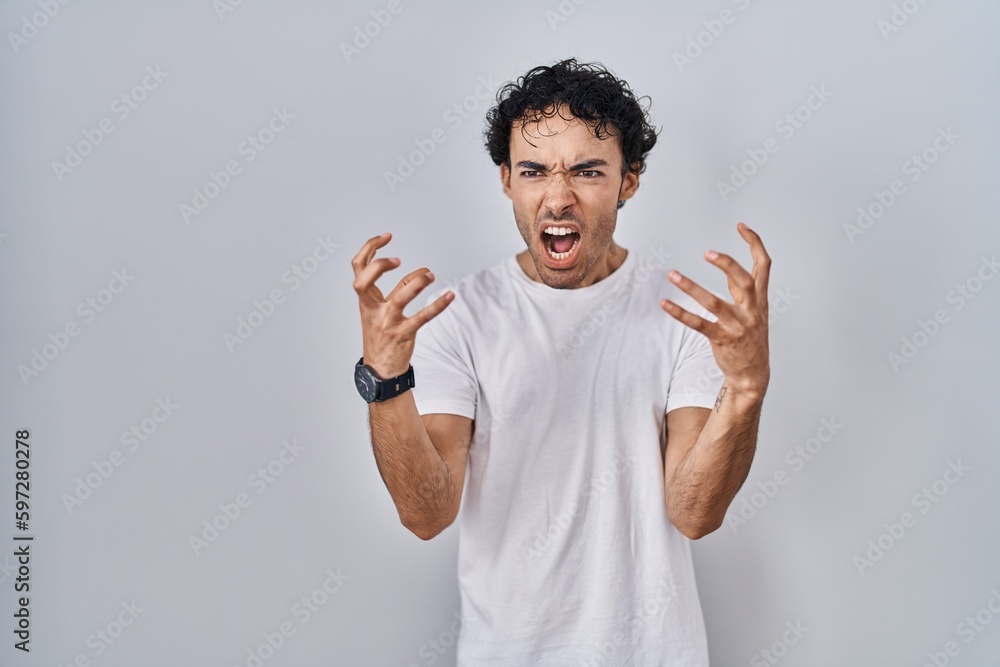 Hispanic man standing over isolated background crazy and mad shouting and yelling with aggressive expression and arms raised. frustration concept. Hispanic man standing over isolated background crazy and mad shouting and yelling with aggressive expression and arms raised. frustration concept.