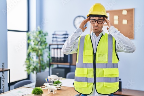 Obraz na plátně Hispanic man wearing architect hardhat with hand on head, headache because stress