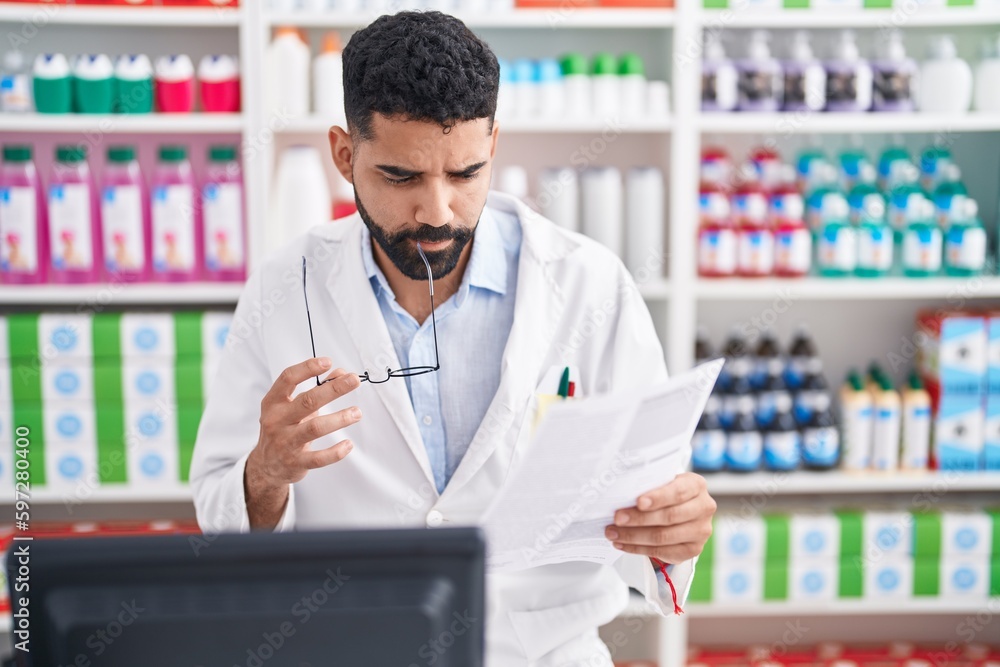 Young arab man pharmacist reading document with doubt expression at pharmacy Young arab man pharmacist reading document with doubt expression at pharmacy