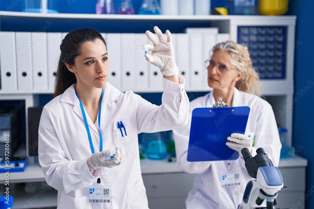 Two women scientists holding pills write on document at laboratory Two women scientists holding pills write on document at laboratory