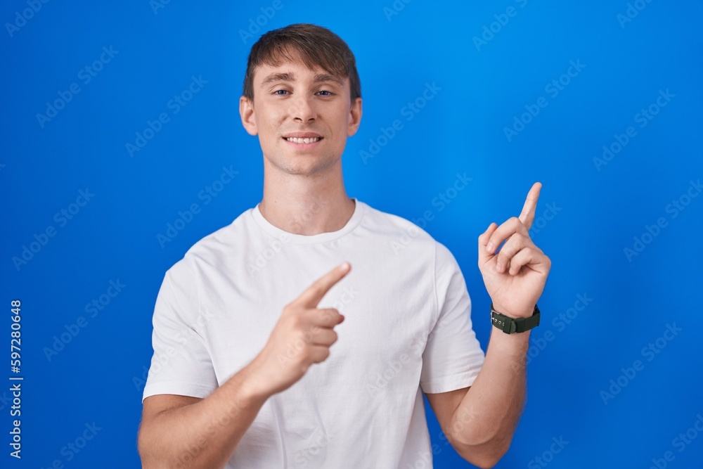 Caucasian blond man standing over blue background smiling and looking at the camera pointing with two hands and fingers to the side. Caucasian blond man standing over blue background smiling and looking at the camera pointing with two hands and fingers to the side.