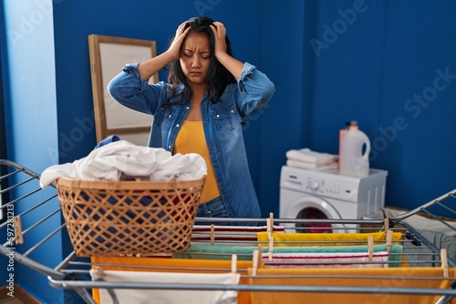 Young asian woman hanging clothes at clothesline suffering from headache desperate and stressed because pain and migraine. hands on head.