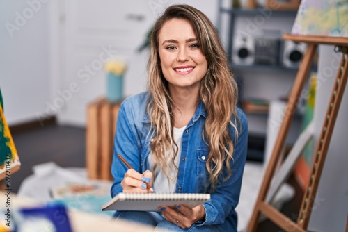 Young woman artist drawing on notebook sitting on floor at art studio