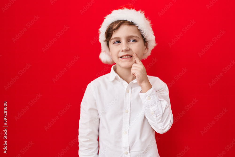 Little caucasian boy wearing christmas hat over red background smiling looking confident at the camera with crossed arms and hand on chin. thinking positive. Little caucasian boy wearing christmas hat over red background smiling looking confident at the camera with crossed arms and hand on chin. thinking positive.