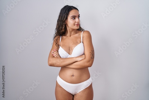 Young hispanic woman wearing white lingerie looking to the side with arms crossed convinced and confident