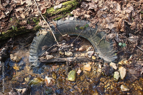 Car tire ingrown halfway into the ground lying in the bed of a stream in nature