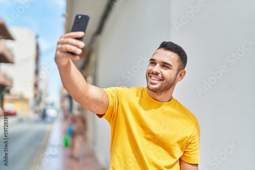 Young hispanic man smiling confident making selfie by the smartphone at street