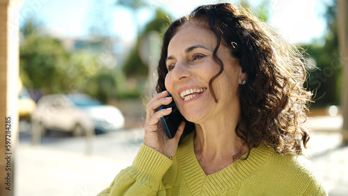 Middle age hispanic woman smiling confident talking on the smartphone at street