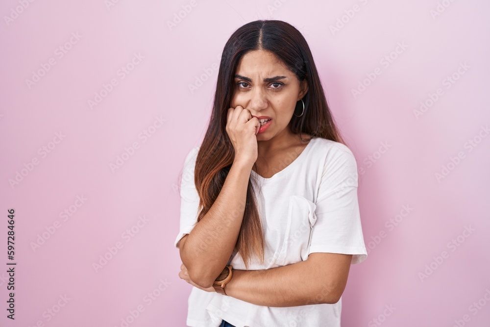 Young arab woman standing over pink background looking stressed and nervous with hands on mouth biting nails. anxiety problem. Young arab woman standing over pink background looking stressed and nervous with hands on mouth biting nails. anxiety problem.