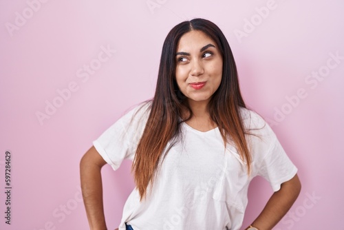 Young arab woman standing over pink background smiling looking to the side and staring away thinking.