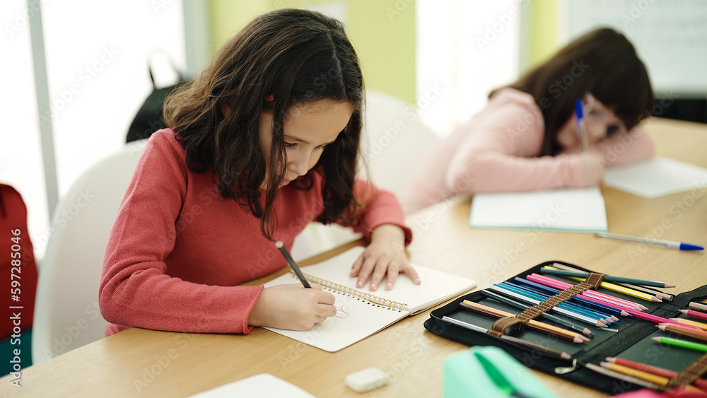 Adorable girls students sitting on table drawing on notebook at classroom Adorable girls students sitting on table drawing on notebook at classroom