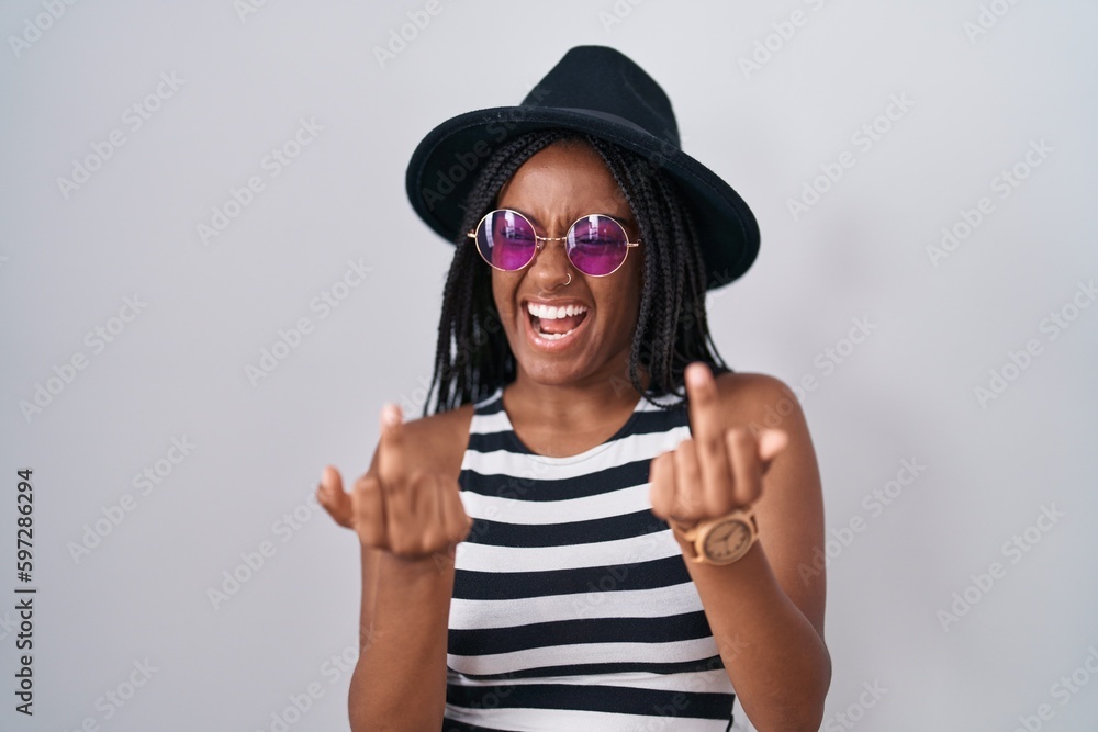 Young african american with braids wearing hat and sunglasses showing middle finger doing fuck you bad expression, provocation and rude attitude. screaming excited Young african american with braids wearing hat and sunglasses showing middle finger doing fuck you bad expression, provocation and rude attitude. screaming excited