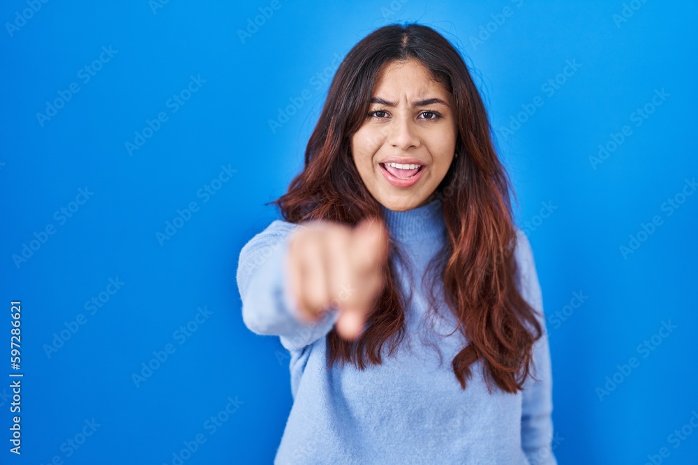 Hispanic young woman standing over blue background pointing displeased and frustrated to the camera, angry and furious with you Hispanic young woman standing over blue background pointing displeased and frustrated to the camera, angry and furious with you