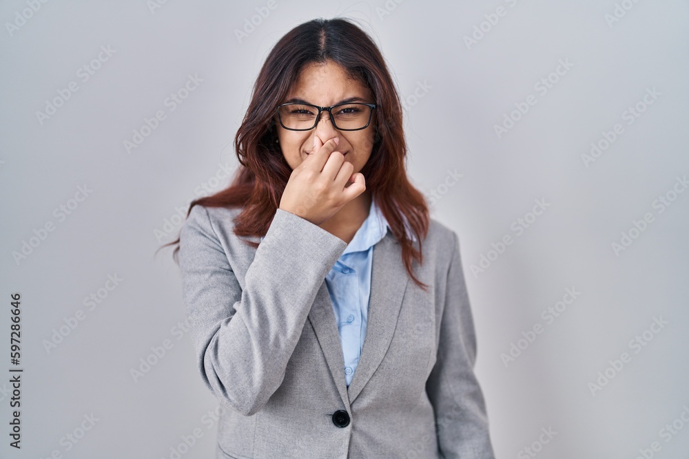 Hispanic young business woman wearing glasses smelling something stinky and disgusting, intolerable smell, holding breath with fingers on nose. bad smell Hispanic young business woman wearing glasses smelling something stinky and disgusting, intolerable smell, holding breath with fingers on nose. bad smell
