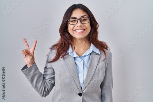 Hispanic young business woman wearing glasses showing and pointing up with fingers number two while smiling confident and happy.