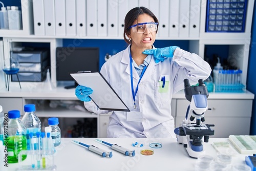 Hispanic young woman working at scientist laboratory cutting throat with hand as knife  threaten aggression with furious violence