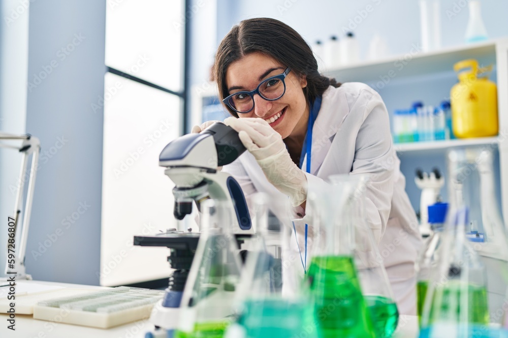 Young hispanic woman wearing scientist uniform using microscope at laboratory Young hispanic woman wearing scientist uniform using microscope at laboratory
