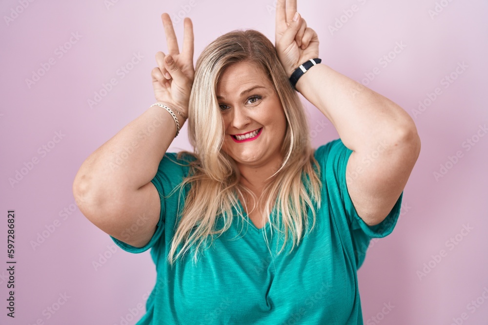 Fototapeta premium Caucasian plus size woman standing over pink background posing funny and crazy with fingers on head as bunny ears, smiling cheerful