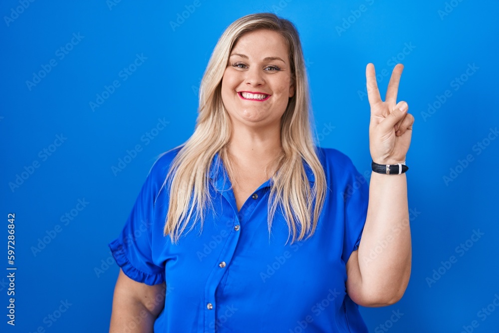 Fototapeta premium Caucasian plus size woman standing over blue background showing and pointing up with fingers number two while smiling confident and happy.