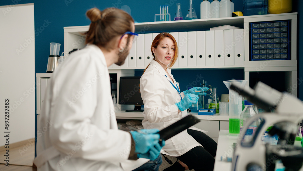 Man and woman wearing sciencist uniform writing on clipboard at laboratory Man and woman wearing sciencist uniform writing on clipboard at laboratory