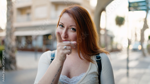 Young redhead woman smiling confident pointing with finger at street