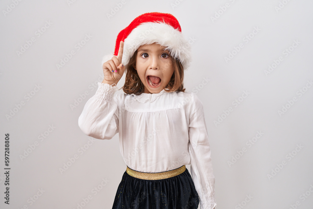 Little hispanic girl wearing christmas hat smiling with an idea or question pointing finger up with happy face, number one Little hispanic girl wearing christmas hat smiling with an idea or question pointing finger up with happy face, number one