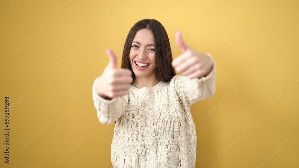 Young beautiful hispanic woman smiling confident doing ok sign with thumbs up over isolated yellow background