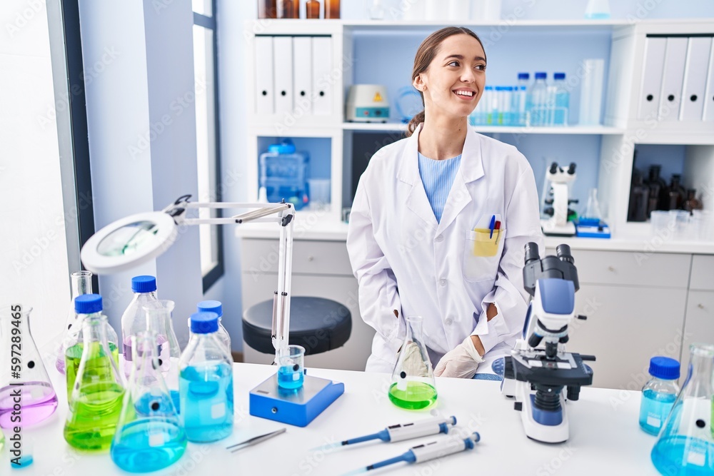 Young brunette woman working at scientist laboratory looking away to side with smile on face, natural expression. laughing confident. Young brunette woman working at scientist laboratory looking away to side with smile on face, natural expression. laughing confident.