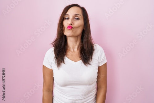 Middle age brunette woman standing over pink background looking at the camera blowing a kiss on air being lovely and sexy. love expression.