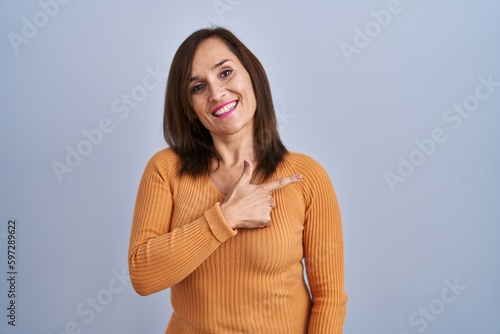 Middle age brunette woman standing wearing orange sweater cheerful with a smile on face pointing with hand and finger up to the side with happy and natural expression © Krakenimages.com