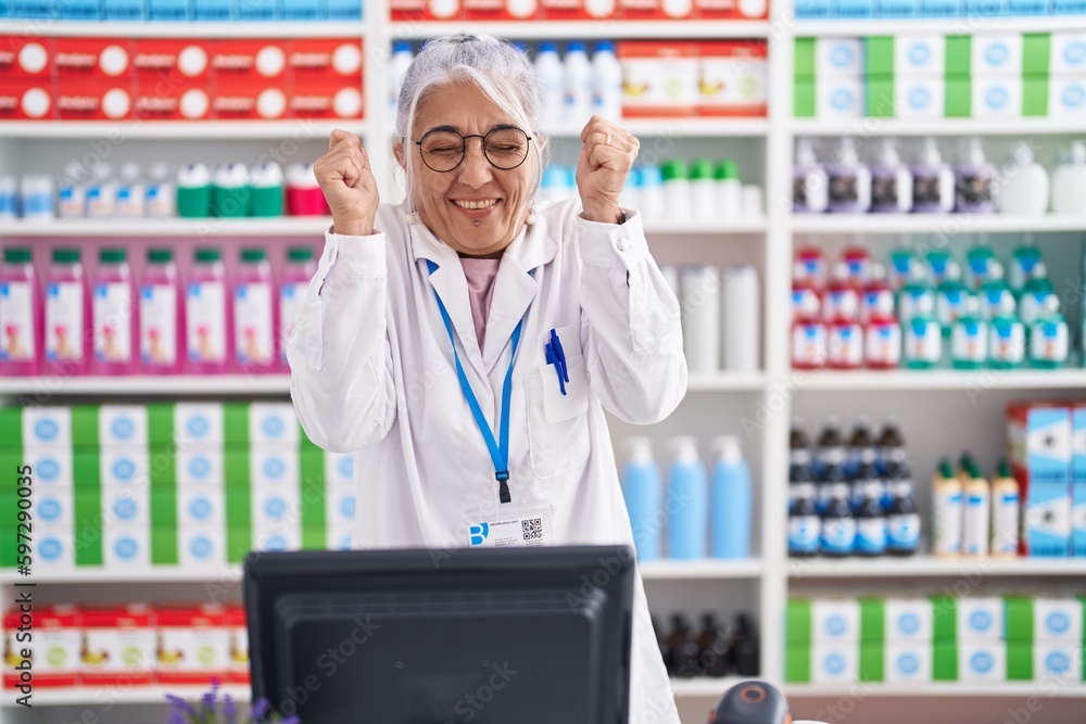 Middle age woman with tattoos working at pharmacy drugstore excited for success with arms raised and eyes closed celebrating victory smiling. winner concept. Middle age woman with tattoos working at pharmacy drugstore excited for success with arms raised and eyes closed celebrating victory smiling. winner concept.