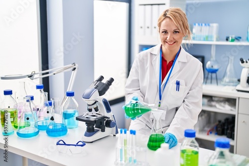 Young blonde woman scientist pouring liquid on test tube at laboratory
