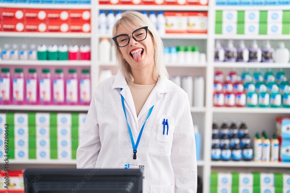 Young caucasian woman working at pharmacy drugstore sticking tongue out happy with funny expression. emotion concept.