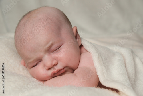 Portrait of newborn baby girl sleeping on her front, covered with a cream blanket.